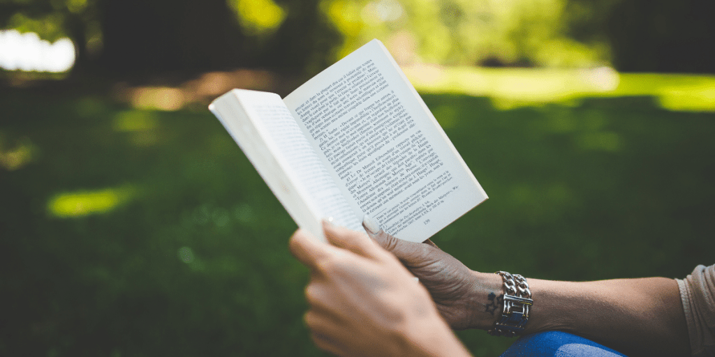 a person reading a book outside in a green park 