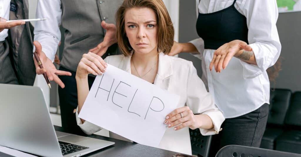 Stressed office worker holding a help sign surrounded by colleagues' demands.