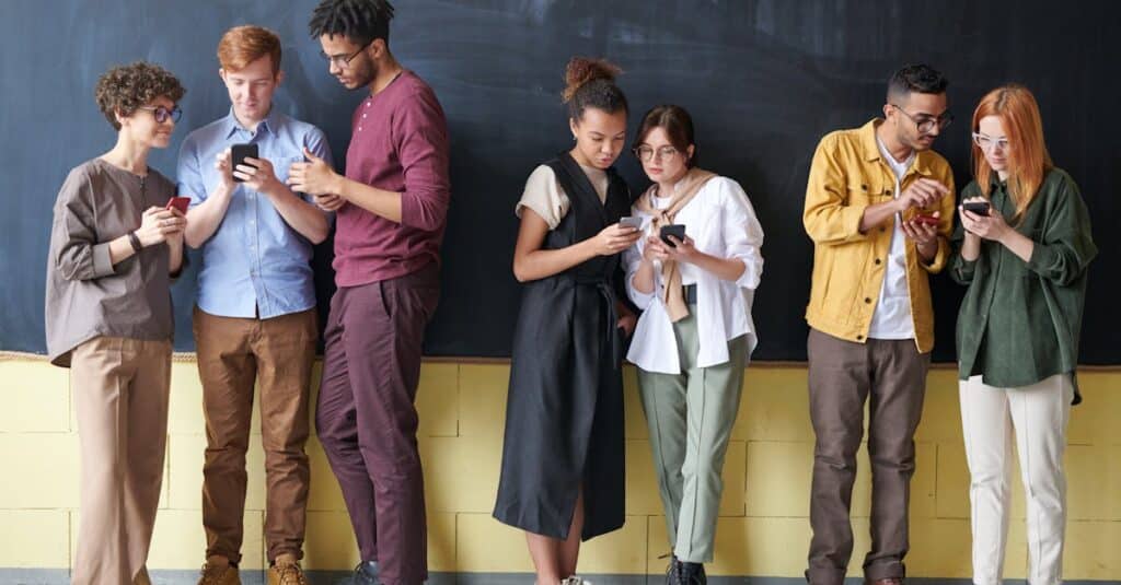 Young diverse adults using smartphones while standing against a blackboard, showcasing technology and connection.