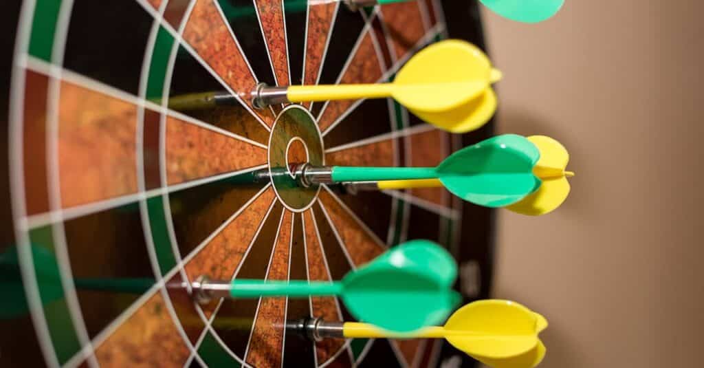 Multiple green and yellow darts precisely hitting a dartboard bullseye, indoor sport scene.
